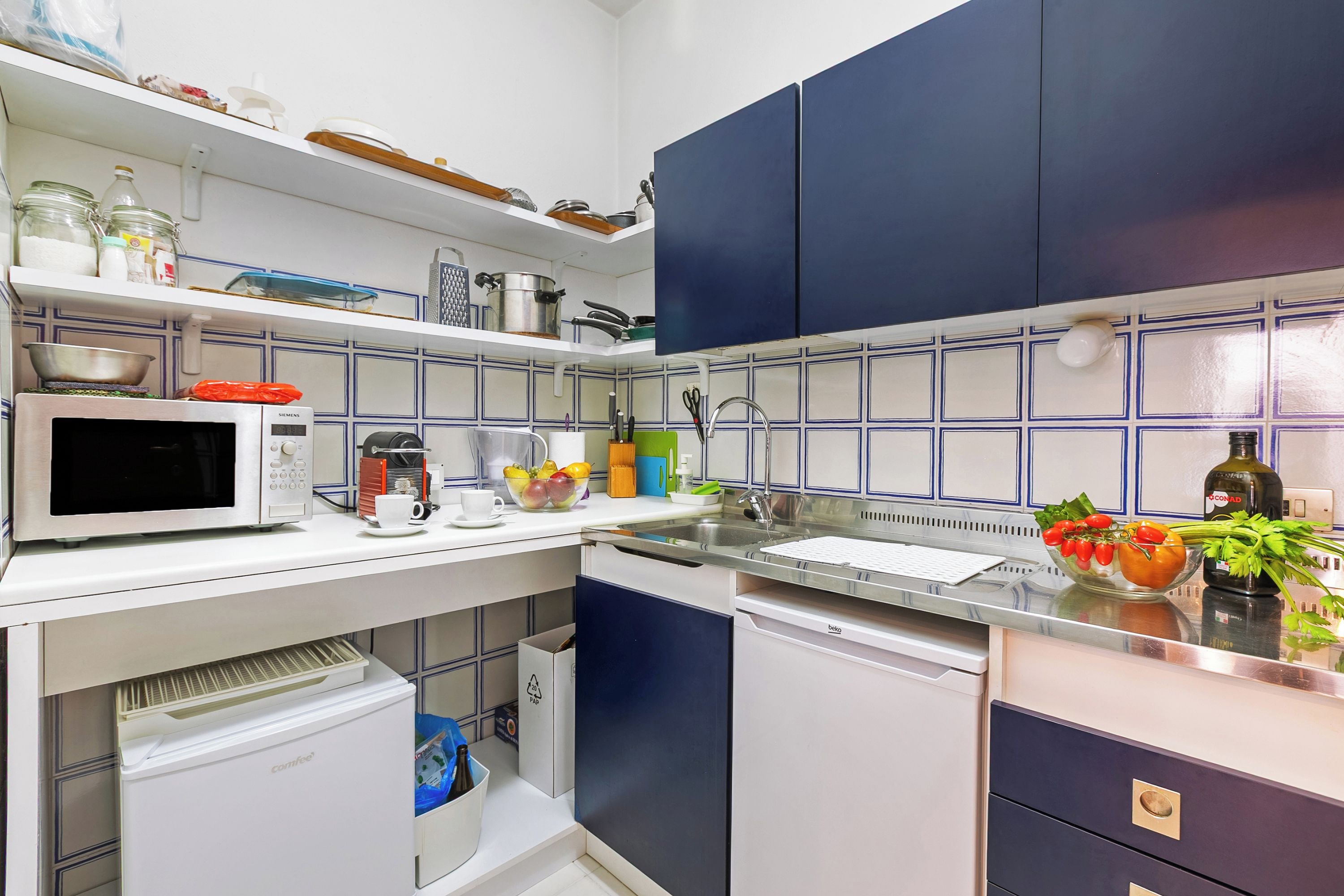 Une cuisine compacte dotée de plans de travail blancs, d’un four à micro-ondes, d’une machine à café et d’un lave-vaisselle.