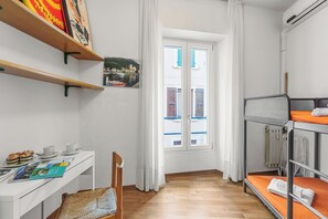 Una stanza con un letto a castello, una scrivania con una sedia, una finestra con tende e uno scaffale con libri e un quadro.