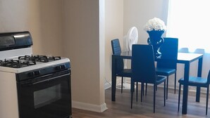 Eine Küche mit Herd und Backofen, ein Essbereich mit Stühlen und Tisch sowie ein Fenster mit Vorhängen.