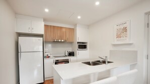 A modern kitchen with white cabinetry, a built-in microwave, and a stainless steel sink. - Ground Level 1-bed: Courtyard & Alfresco Dining (Canberra)