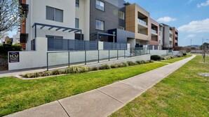 A modern multi-story residential building with a flat roof, large windows, and a well-maintained lawn. - Ground Level 1-bed: Courtyard & Alfresco Dining (Canberra)