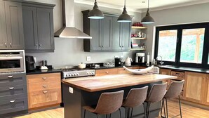 A modern kitchen with a central island, bar stools, and a view of the outdoors through a window.