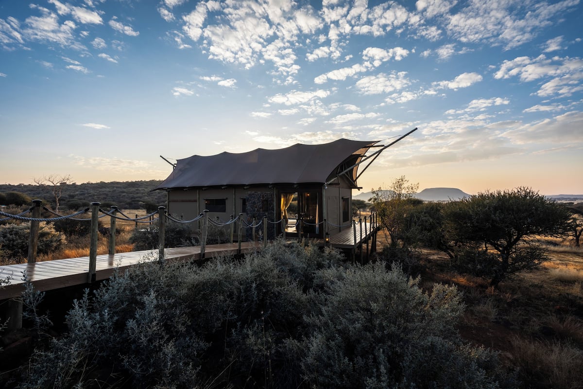 A secluded lodge with a wooden deck and a thatched roof, surrounded by dense shrubbery and a clear sky.
