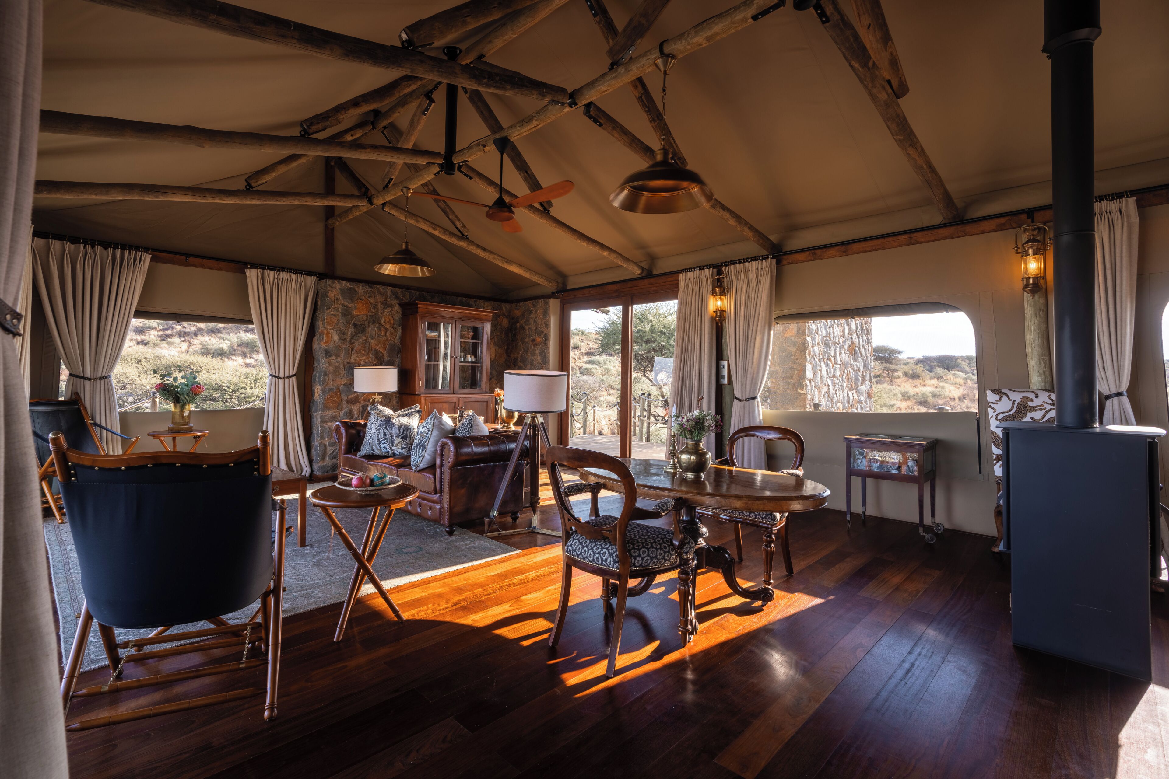 A tented room with wooden floors, a dining table, chairs, a sofa, and a fireplace.