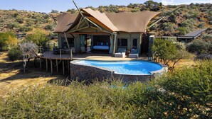Eine Lodge im Wüstendesign mit Pool, Sitzgelegenheiten im Freien und Blick auf die umliegende Landschaft.