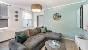A modern living room with a sectional sofa, a round coffee table, a wall clock, and a pendant light. - Holiday Home 'Radlerrast' with Private Garden and Wi-Fi (Weißenfels)