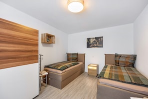 Una habitación compacta con una cama, una mesita pequeña, un armario y un estante en la pared.