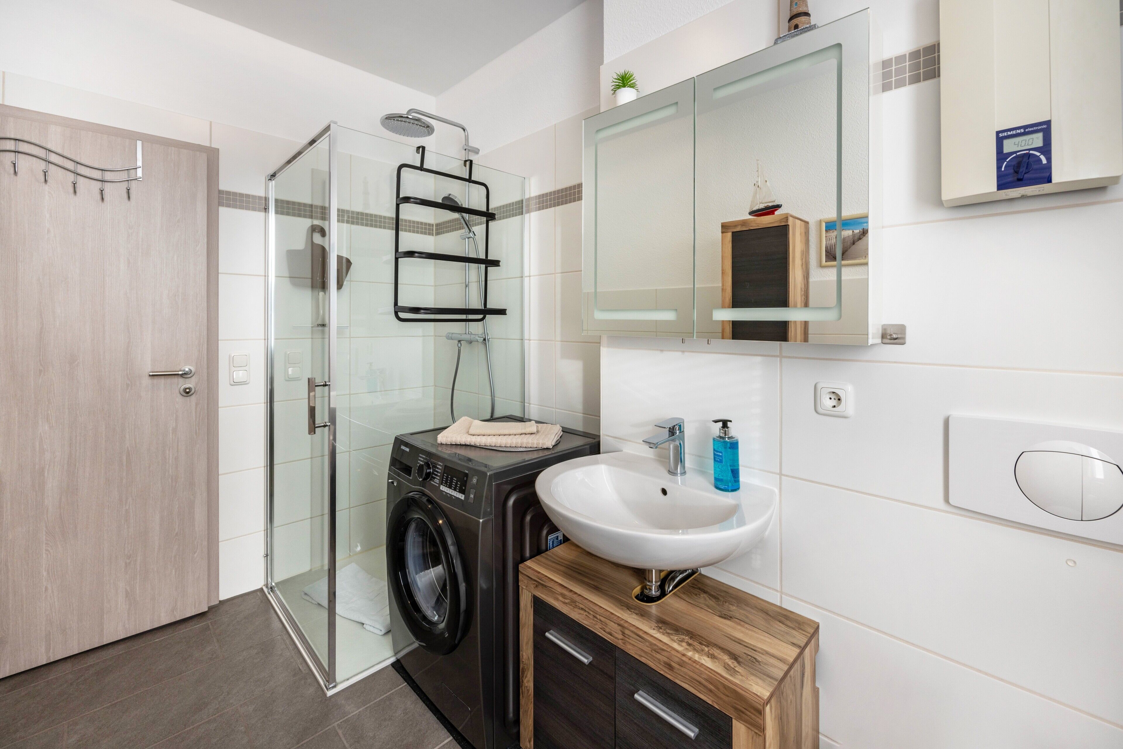 A modern bathroom with a glass shower enclosure, a built-in washing machine, a sink, and a wooden cabinet.