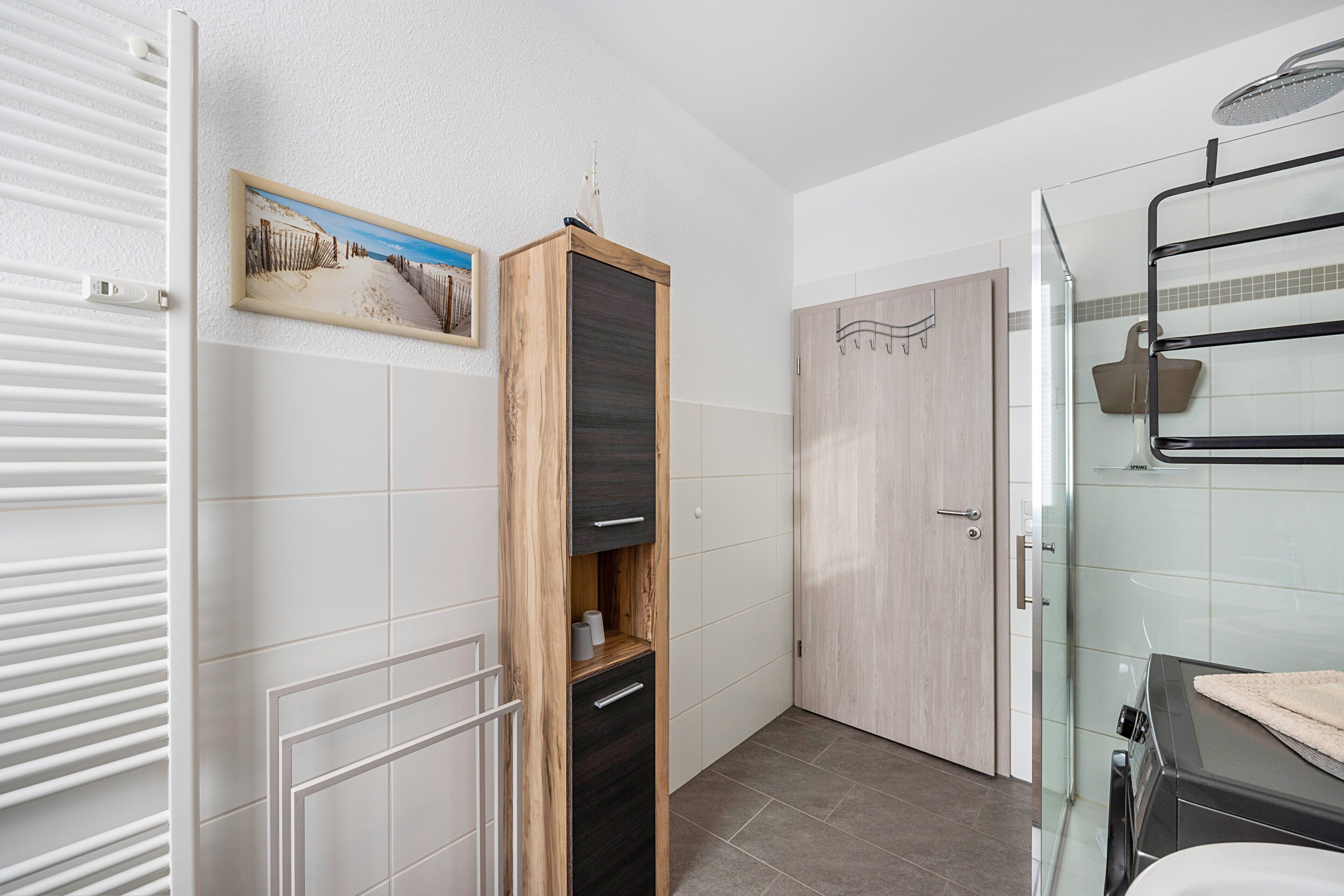 Een badkamer met een douche, een handdoekhouder, een houten kastje en een foto aan de muur.
