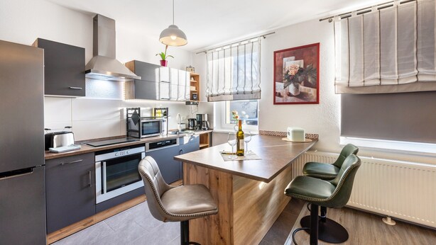 A modern kitchen with a central island, stainless steel appliances, and a green bar stool. - Holiday Home 'Radlerrast' with Private Garden and Wi-Fi (Weißenfels)
