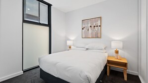 Une chambre moderne avec un grand lit, deux tables de chevet avec des lampes, une fenêtre et un tableau abstrait accroché au mur.