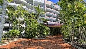 Un hôtel à plusieurs étages doté de balcons, de palmiers et d’un chemin bordé de briques.