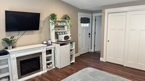 A living room with a fireplace, a flat-screen TV mounted on the wall, a white entertainment unit, a microwave, and a small refrigerator. - Private room and bathroom in safe Vancouver neighborhood (Vancouver)