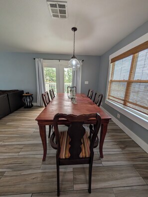 A dining room with a wooden table, chairs, a hanging light fixture, and a large window with a view.