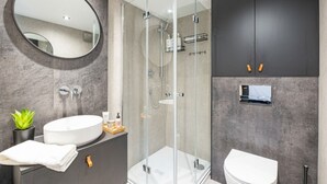 A modern bathroom with a glass-enclosed shower, a round mirror, a sink, and a toilet. - Romantic Geodesic Dome • Hot Tub Under the Stars (pipestem)