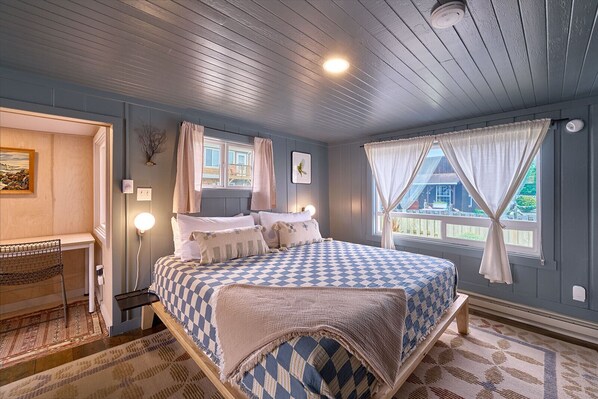 A bedroom with a bed, bedside table, lamp, and a view of the outside. - Remodeled | Downtown Long Beach (The Nest) (Long Beach)