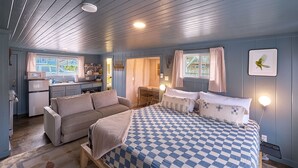 Une chambre confortable avec une couvre-lit à carreaux, un canapé et, au fond, un coin cuisine.
