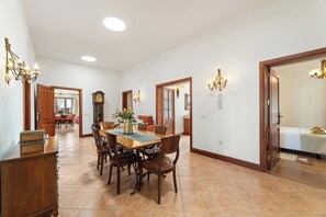 A spacious dining area with a wooden table and chairs, a chandelier, and a clock on the wall.