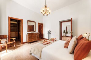 A bedroom with a bed, wooden furniture, a dresser, a mirror, and a chandelier.