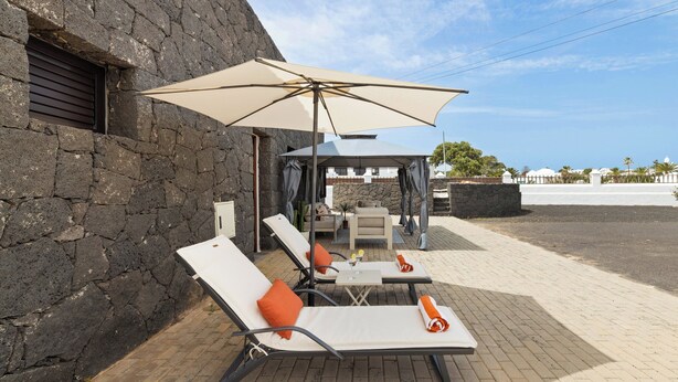 A patio with lounge chairs, a table, and a large umbrella. - Refugio del Volcán by Tropical Host (Uga)