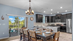 A modern kitchen with dark cabinets, stainless steel appliances, and a dining area with a large island and chairs. - Ohana Memories At Championsgate (Four Corners)