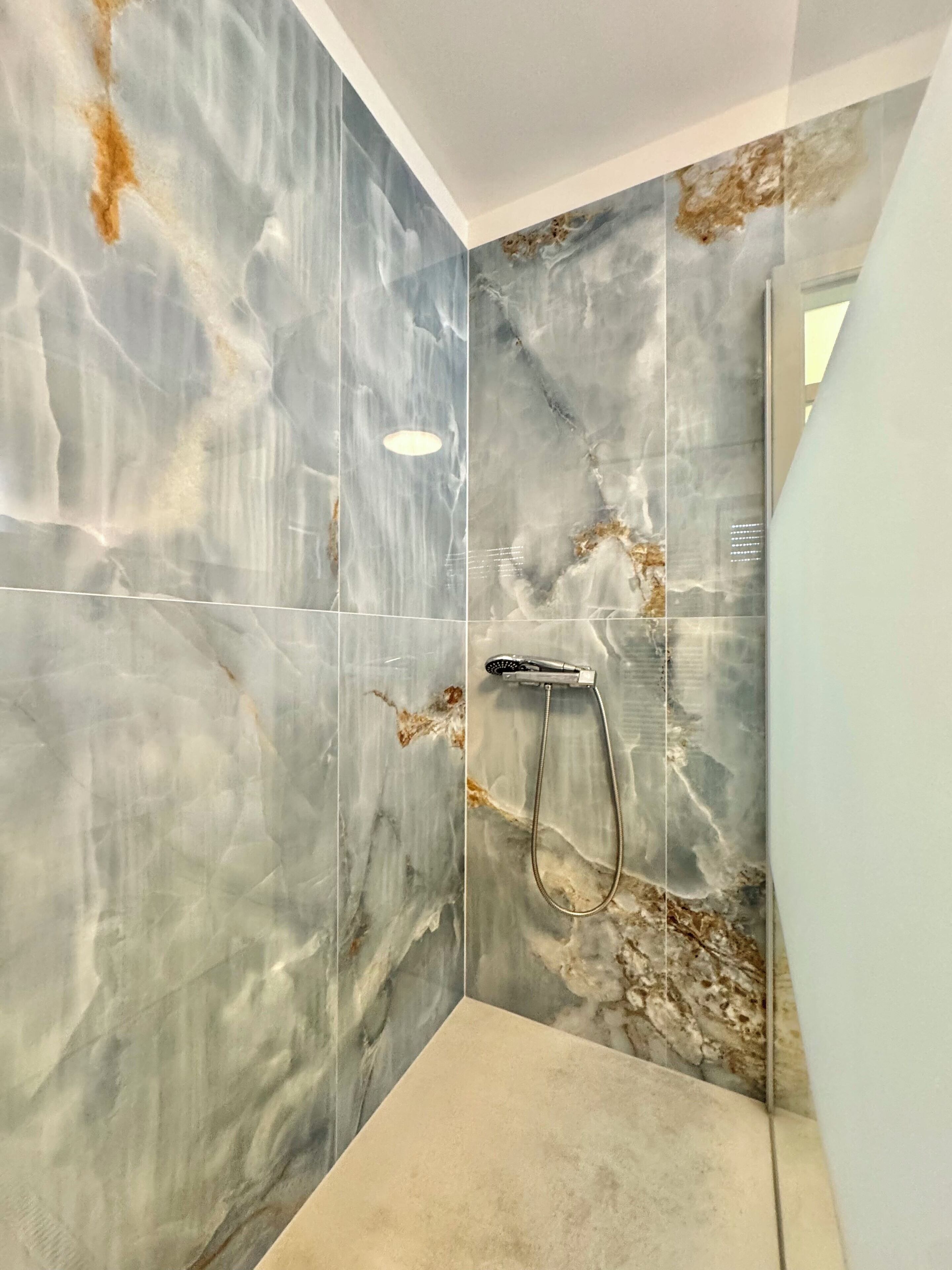 Une salle de bain moderne avec une douche, des murs en marbre et un sol de couleur claire.