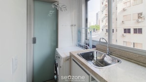 Una cocina compacta con lavadora integrada, un lavabo y una ventana con vistas a un paisaje urbano.
