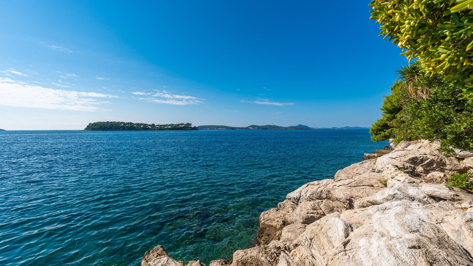 A coastal landscape with clear blue waters, rocky shores, and a distant island.