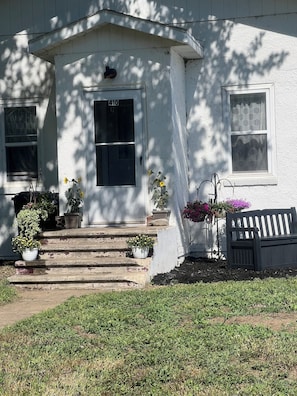 A white house with a number '410' on the door, steps leading up to the entrance, and potted plants on the porch.