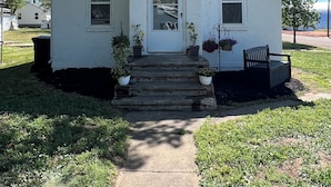 A white single-story house with a front door, two windows, and a small porch with steps.