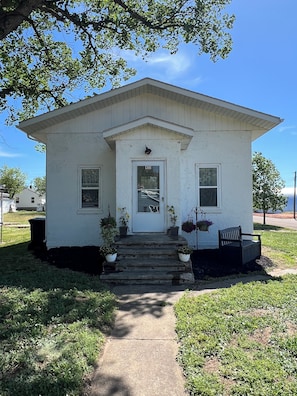 A white single-story house with a front door, two windows, and a small porch with steps.