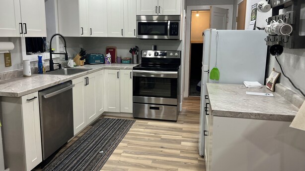 A modern kitchen with white cabinets, stainless steel appliances, and a wooden floor.