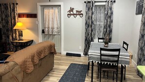A cozy living room with a sofa, a dining table with chairs, a lamp, and a patterned rug.