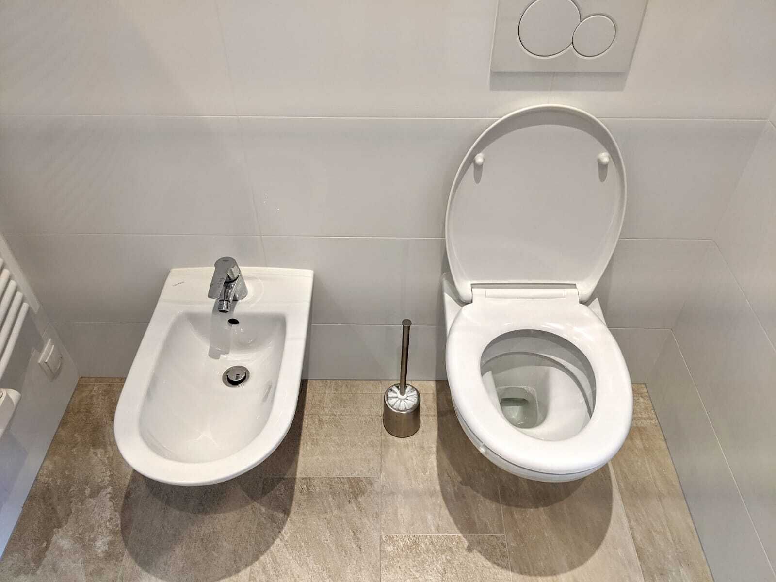A bathroom with a bidet, a toilet, and a hand dryer.