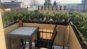 Ein Balkon mit Tisch und Stühlen, der auf einen von einer Mauer umgebenen Garten mit Bäumen und eine entfernte Ansicht von Gebäuden blickt.