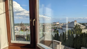 Ein Zimmer mit großem Fenster und Blick auf eine Stadtlandschaft, darunter ein markantes, schlösselartiges Gebäude.