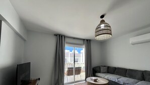 A modern living room with a flat-screen TV, a wooden coffee table, a sofa, and a large window with curtains. - STAY Paradise Apartment (Protaras)