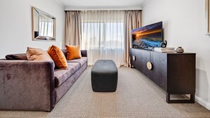 A modern hotel room with a sofa, ottoman, and a cabinet with a flat-screen TV. - Center 1-bed With Sauna, Gym, BBQ & Parking (Canberra)