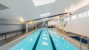 A long indoor swimming pool with clear lanes, benches along the sides, and overhead lighting. - Center 1-bed With Sauna, Gym, BBQ & Parking (Canberra)