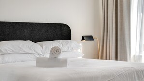 A neatly made bed with white linens and a rolled towel, a black textured headboard, and a modern floor lamp. - Center 1-bed With Sauna, Gym, BBQ & Parking (Canberra)