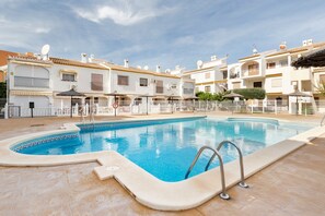 A swimming pool with a tiled deck, surrounded by multi-story buildings with balconies and satellite dishes.
