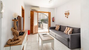Un salon comprenant un canapé, une table basse, un téléviseur et une porte donnant sur un balcon extérieur.