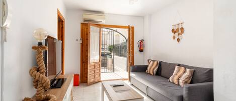 A living room with a sofa, a coffee table, a TV, and a door leading to an outdoor balcony.