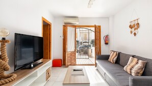 Un salon équipé d’un téléviseur à écran plat, d’une table basse, d’un canapé avec des coussins à motifs, d’une porte en bois et d’un appareil de climatisation.