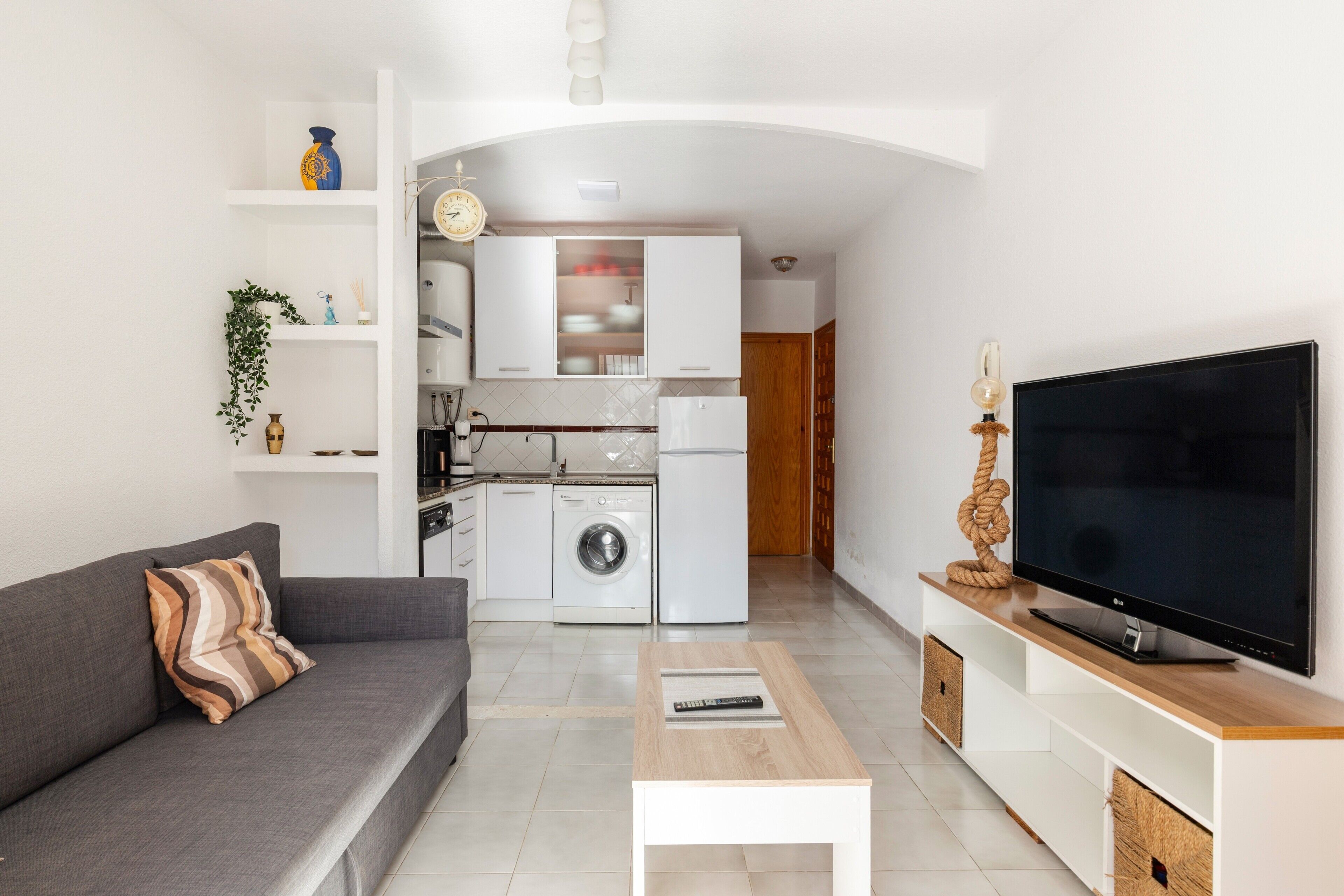 Un espacio habitable compacto con sofá, televisor, cocina equipada y zona de comedor.