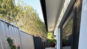 A small patio area with a wooden table and benches, surrounded by a low wooden fence and potted plants. - Cosy Kambah 1 Bedroom Near Shops & Parks (Canberra)