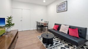 A modern living room with a black sofa, a wooden coffee table, a dining table with chairs, and a potted plant. - Cosy Kambah 1 Bedroom Near Shops & Parks (Canberra)