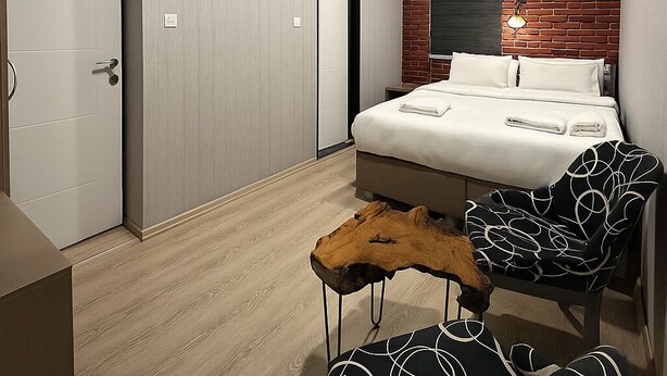 A modern bedroom with a bed, a wooden coffee table, a chair, and a brick accent wall. - Central Stay (İstanbul)