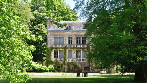 A large stone building with a balcony, surrounded by lush greenery and a pond. - Manoir de Plaisance (Benon)