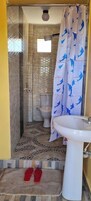 Un baño con cortina de ducha, inodoro, lavamanos y un par de pantuflas sobre un tapete.